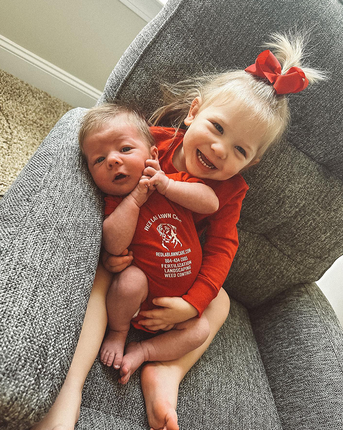 A little girl is holding a newborn baby in her arms.