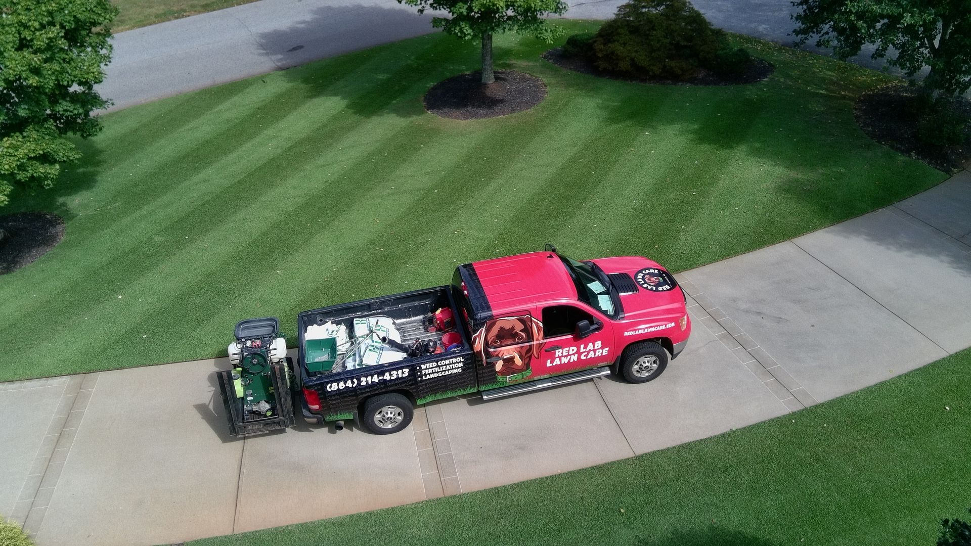An aerial view of a red truck driving down a sidewalk next to a lush green lawn.
