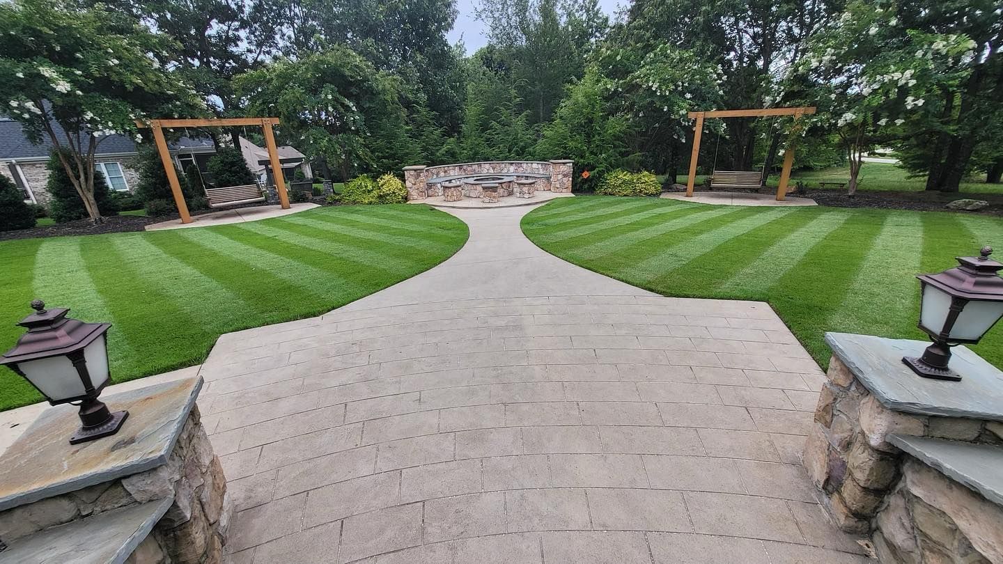 A brick walkway leading to a large lush green lawn.