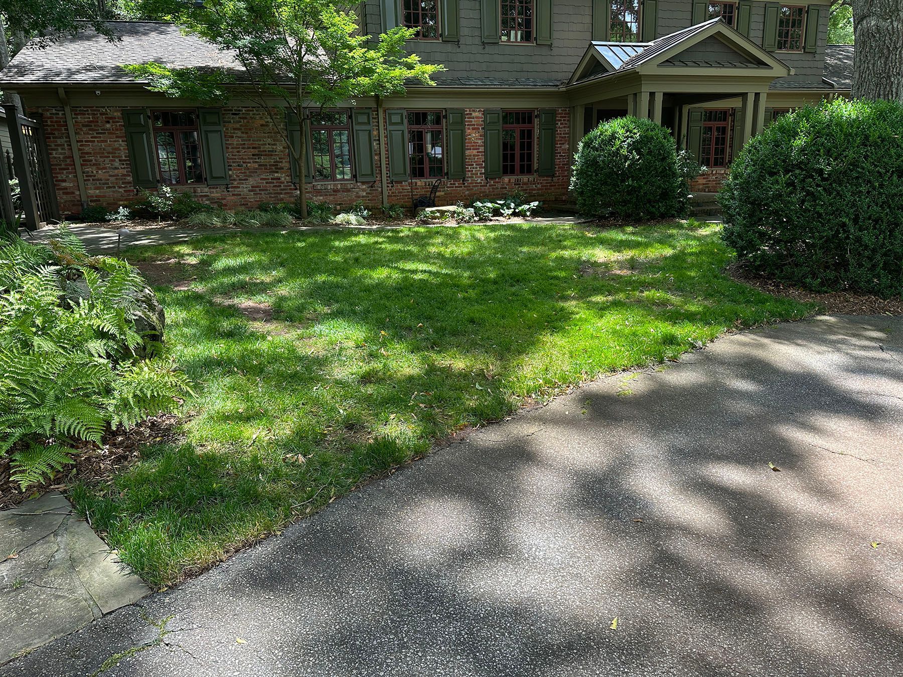 A large brick house with a lush green lawn and a driveway leading to it.