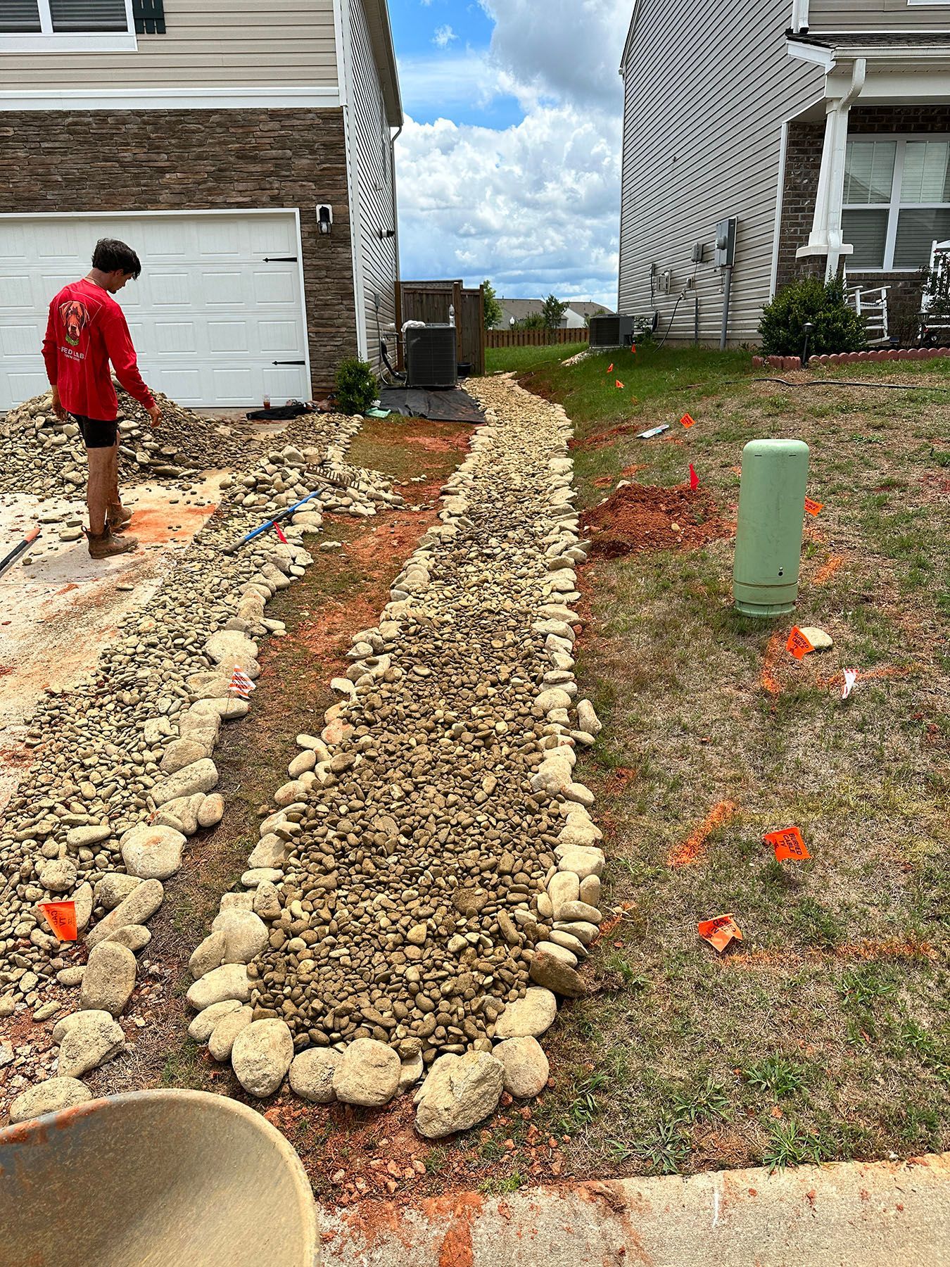 A man is standing next to a pile of rocks in front of a house.