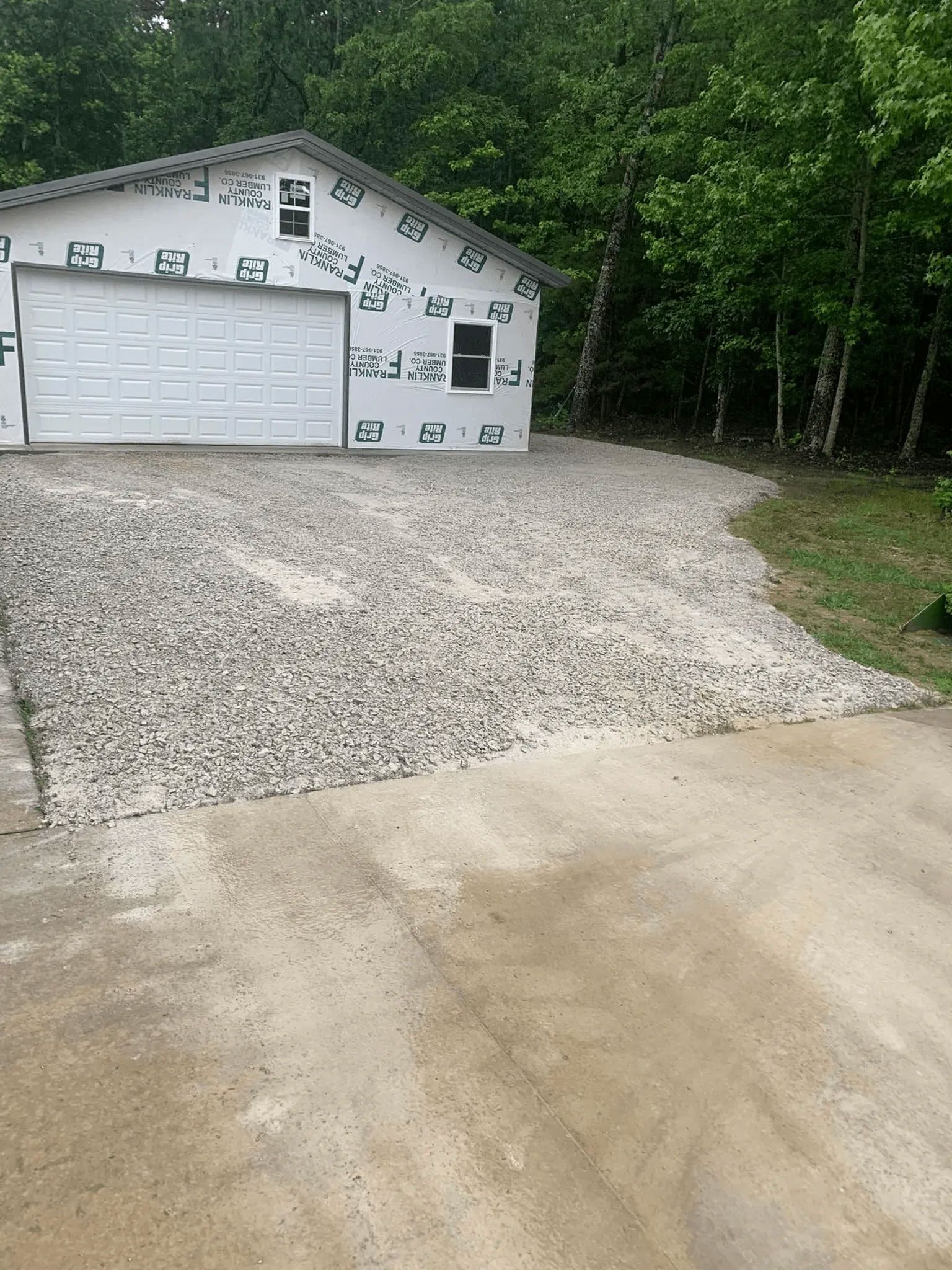 White garage under construction with stone driveway and gravel path in a wooded area