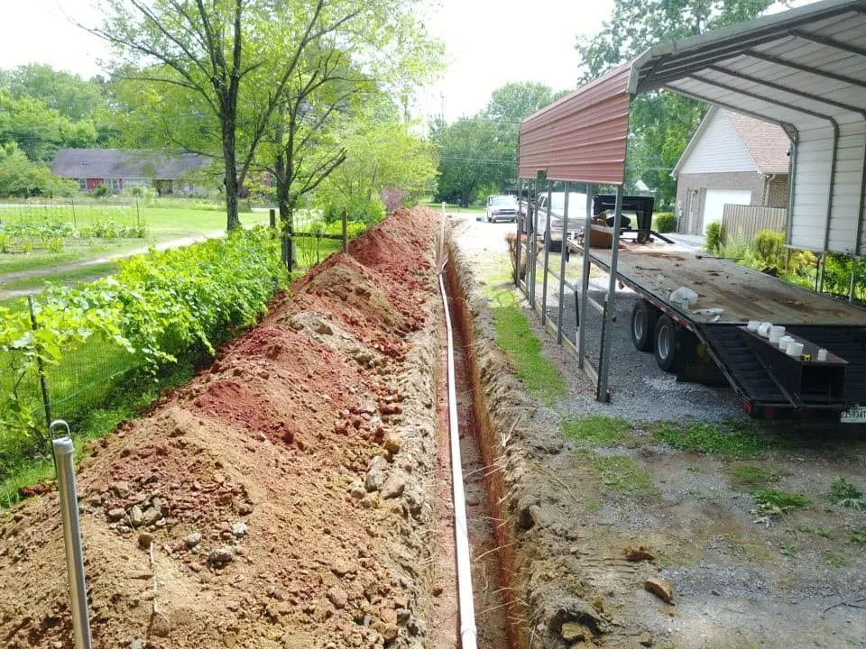 Backyard trench beside a house and carport, with piled dirt and a long narrow excavation.