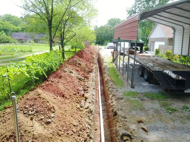 Backyard trench beside a house and carport, with piled dirt and a long narrow excavation.