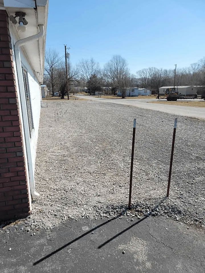 Gravel lot beside a building with two metal stakes in the foreground and bare trees in the distance