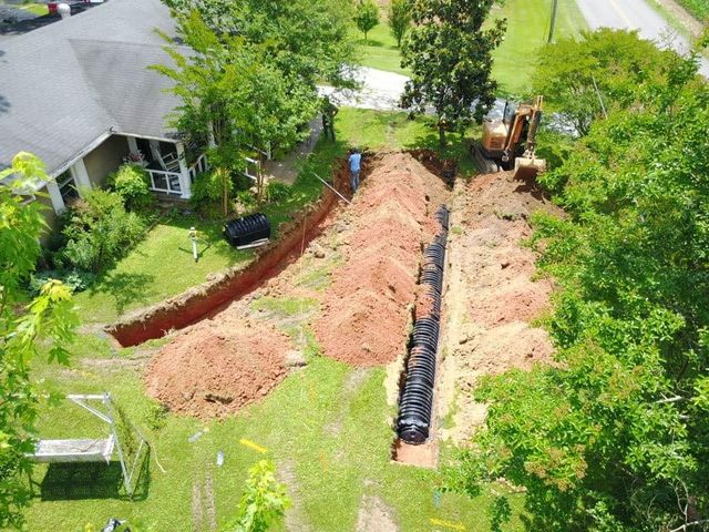 Aerial view of a long trench with black pipes being installed beside a house in a green yard.