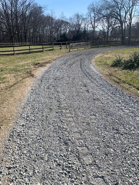 Gravel path curving through a grassy field with bare trees and a wooden fence on a sunny day