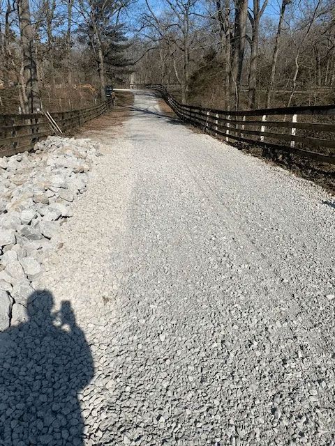 Gravel trail on a wooden bridge in a wooded area, with bare trees and winter debris along the sides.