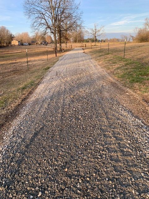 Gravel road through a rural field with leafless trees in warm late-afternoon light