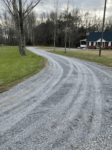 Gravel driveway curving past a house and bare trees on a cloudy day