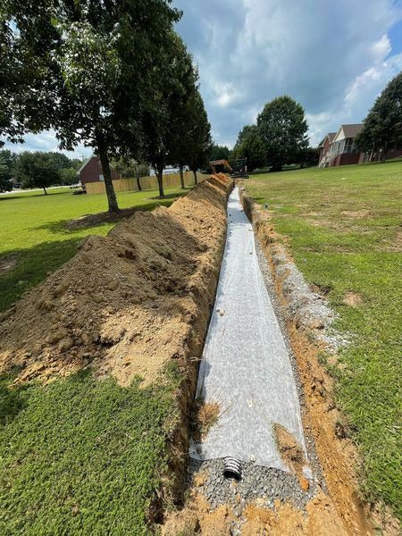 Long concrete drainage trench under construction beside a grassy field and trees