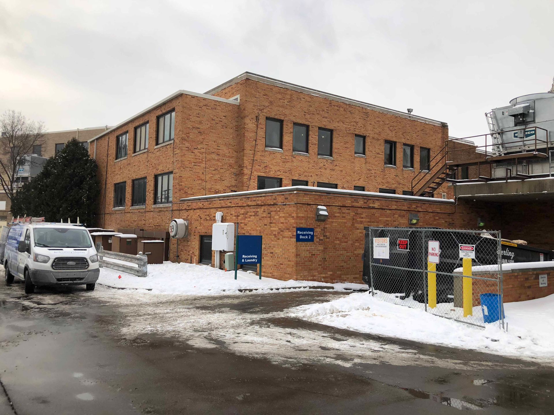 A white van is parked in front of a large brick building.