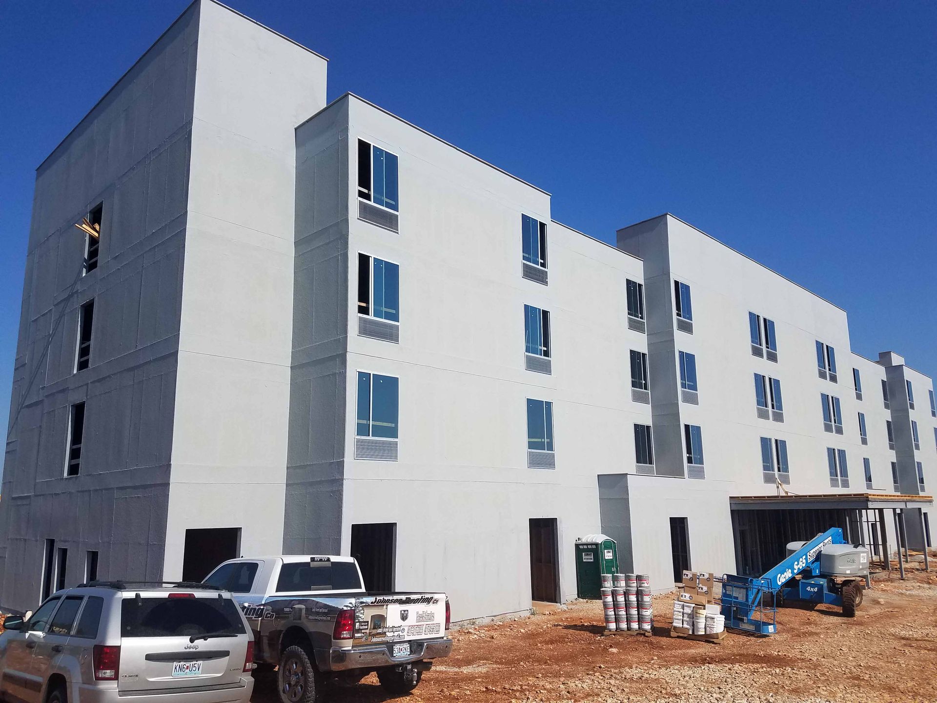 A large white building under construction with cars parked in front of it.