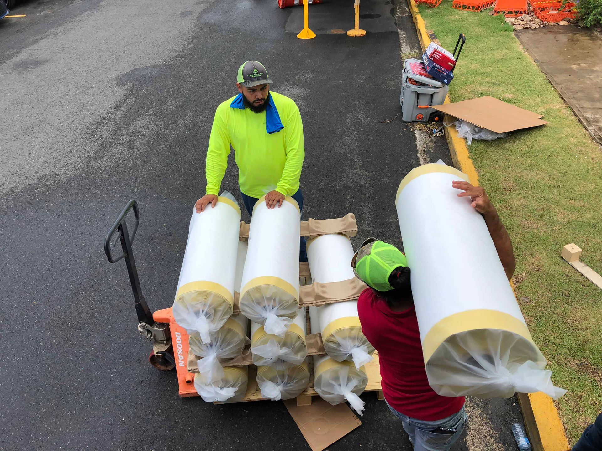 Two men are carrying rolls of insulation on a pallet.