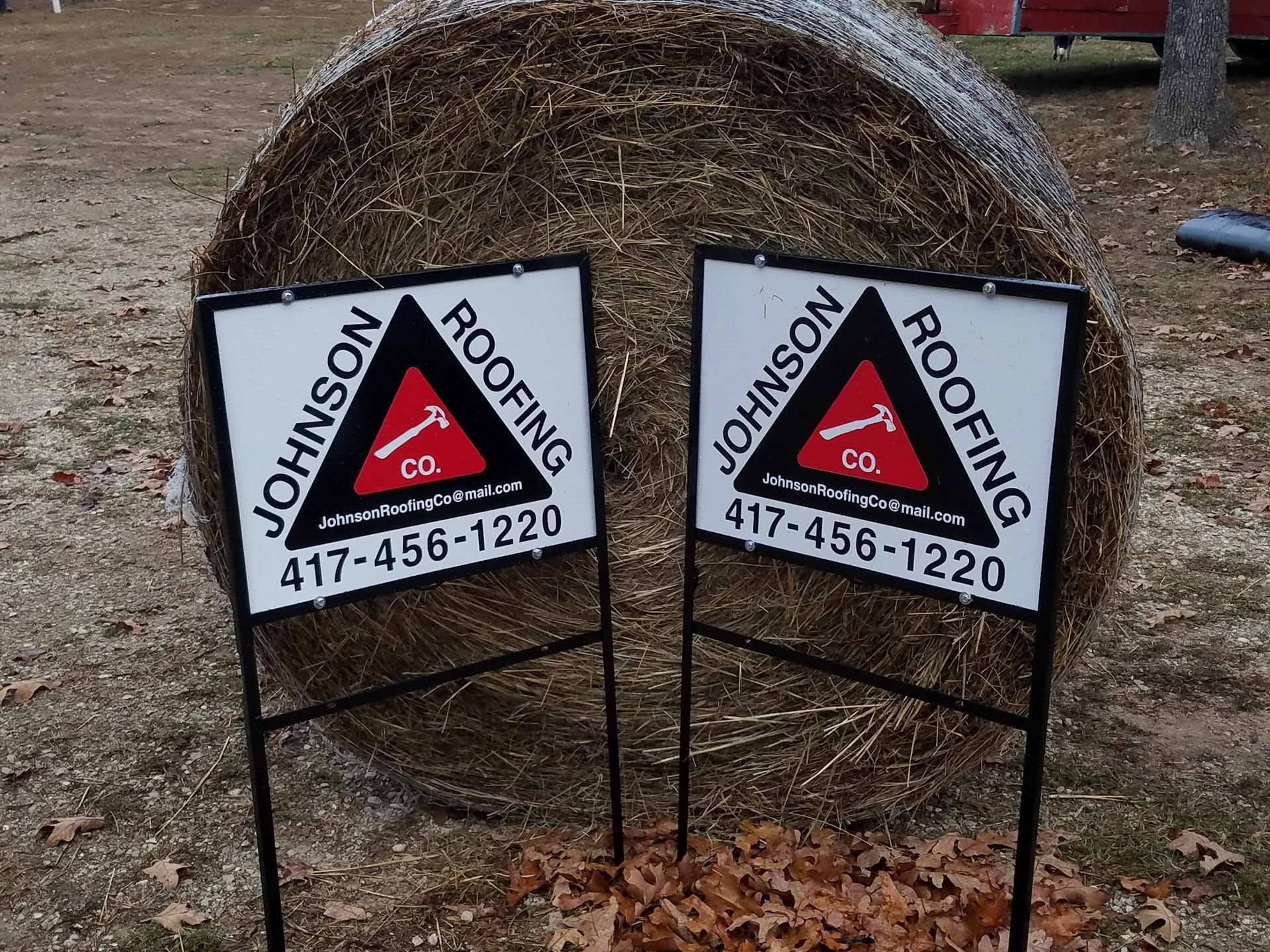 Two signs for johnson roofing sit in front of a bale of hay