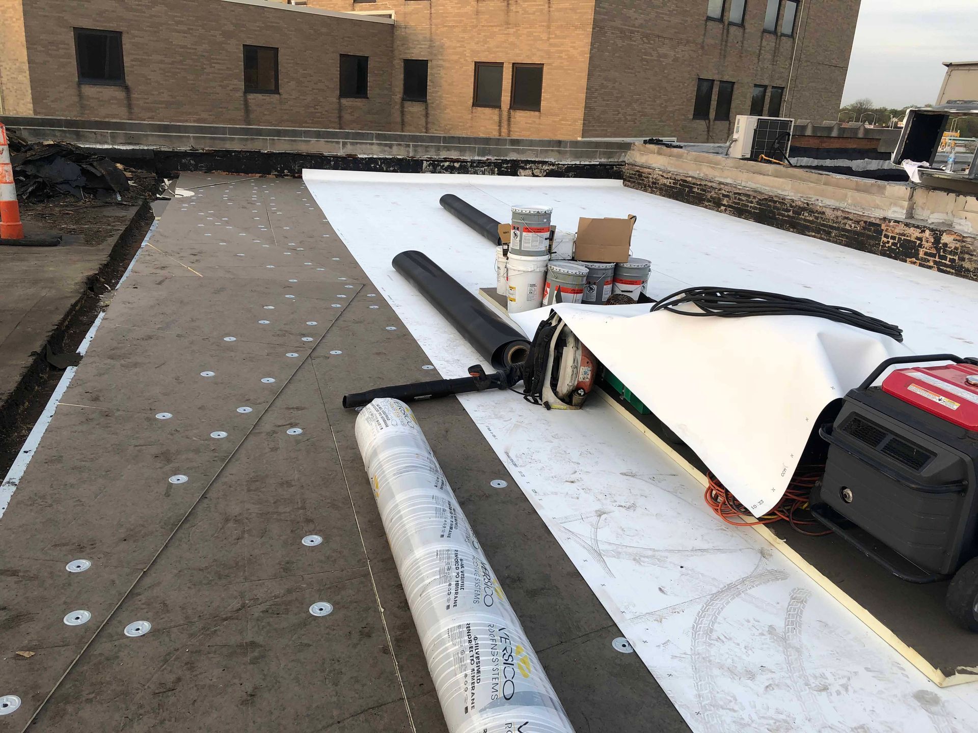 A roof with rolls of roofing material and a generator on it.