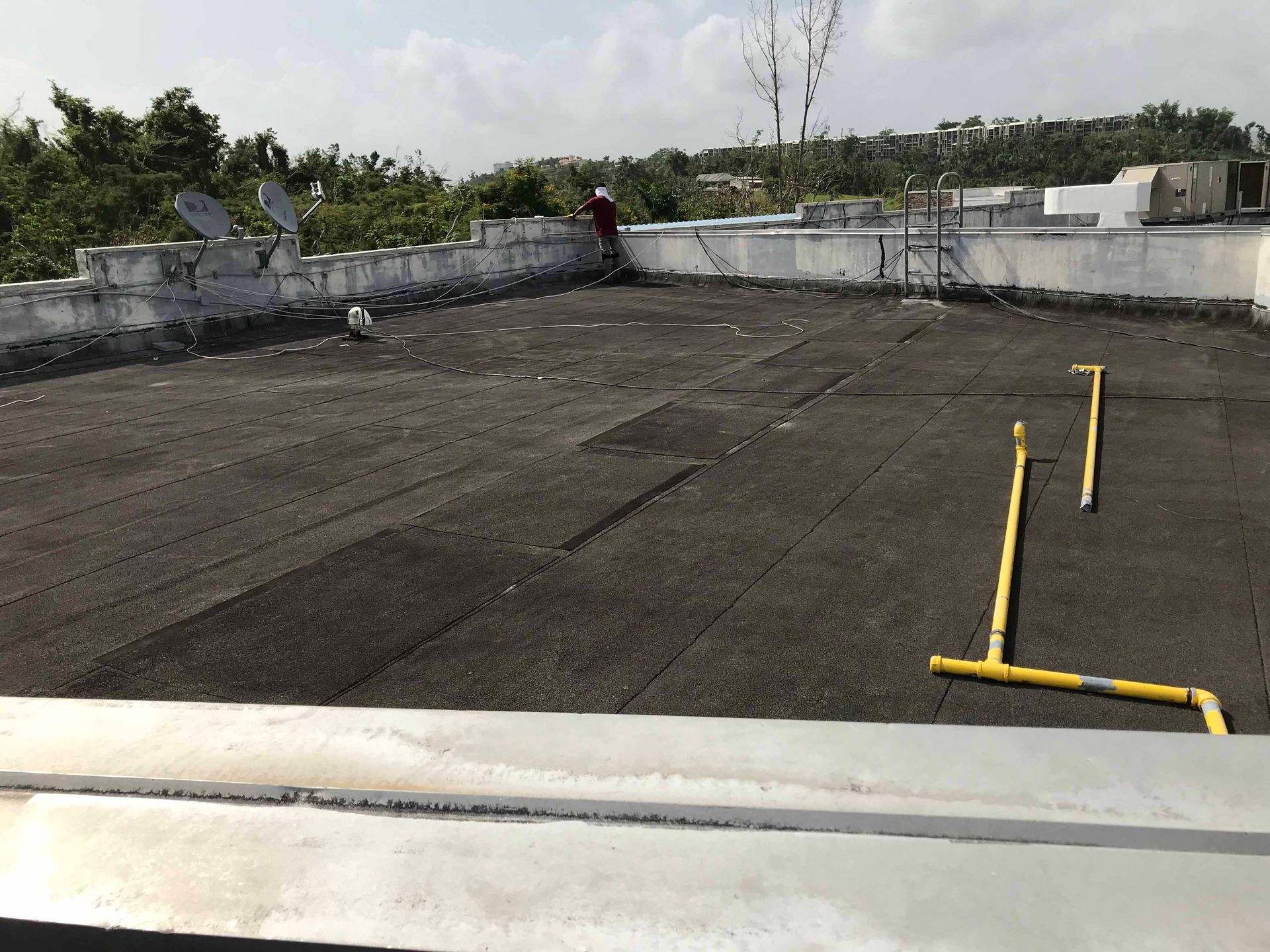 A person is standing on a roof with a yellow pipe.