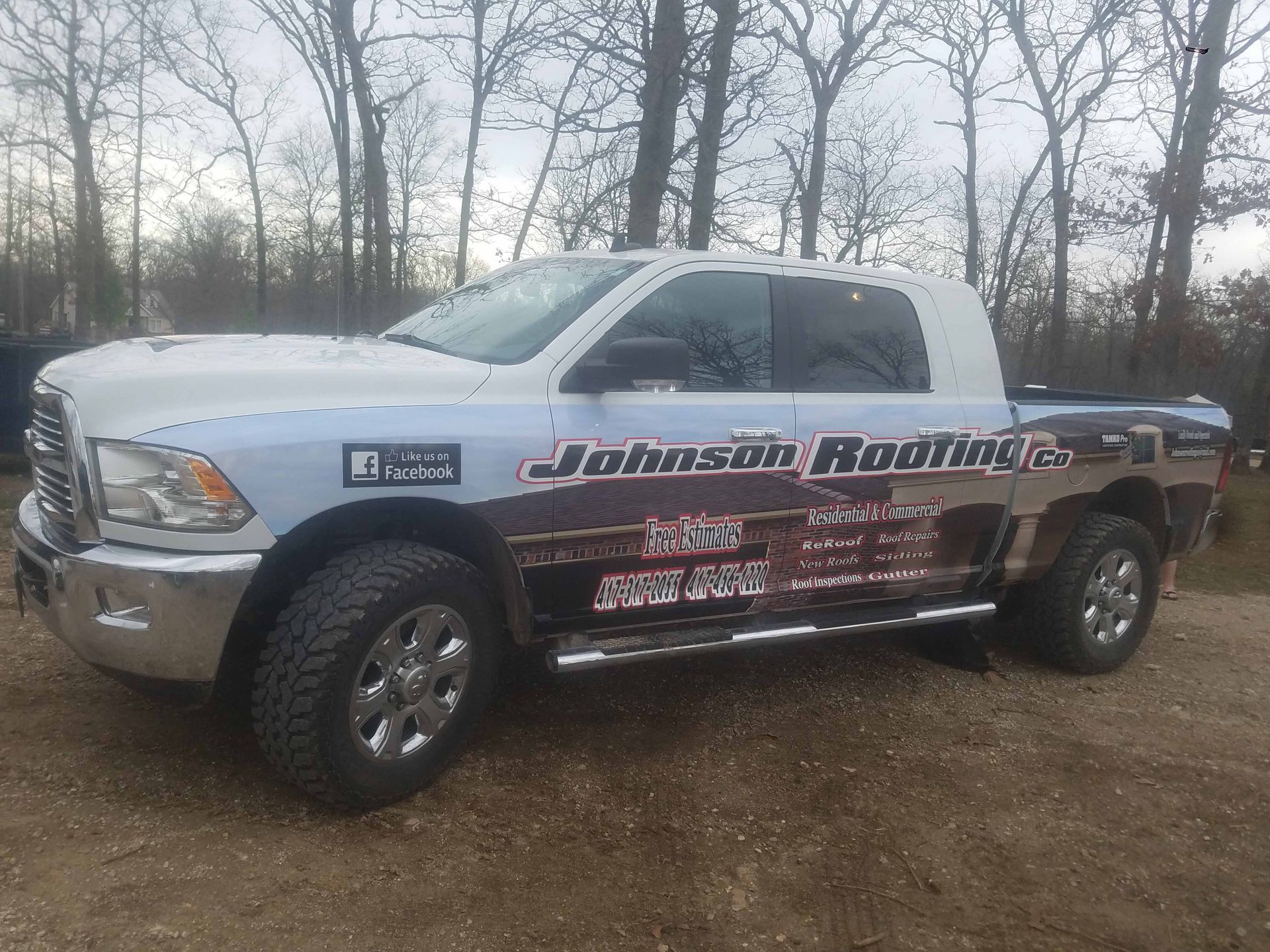 A white truck is parked in a dirt lot with trees in the background.