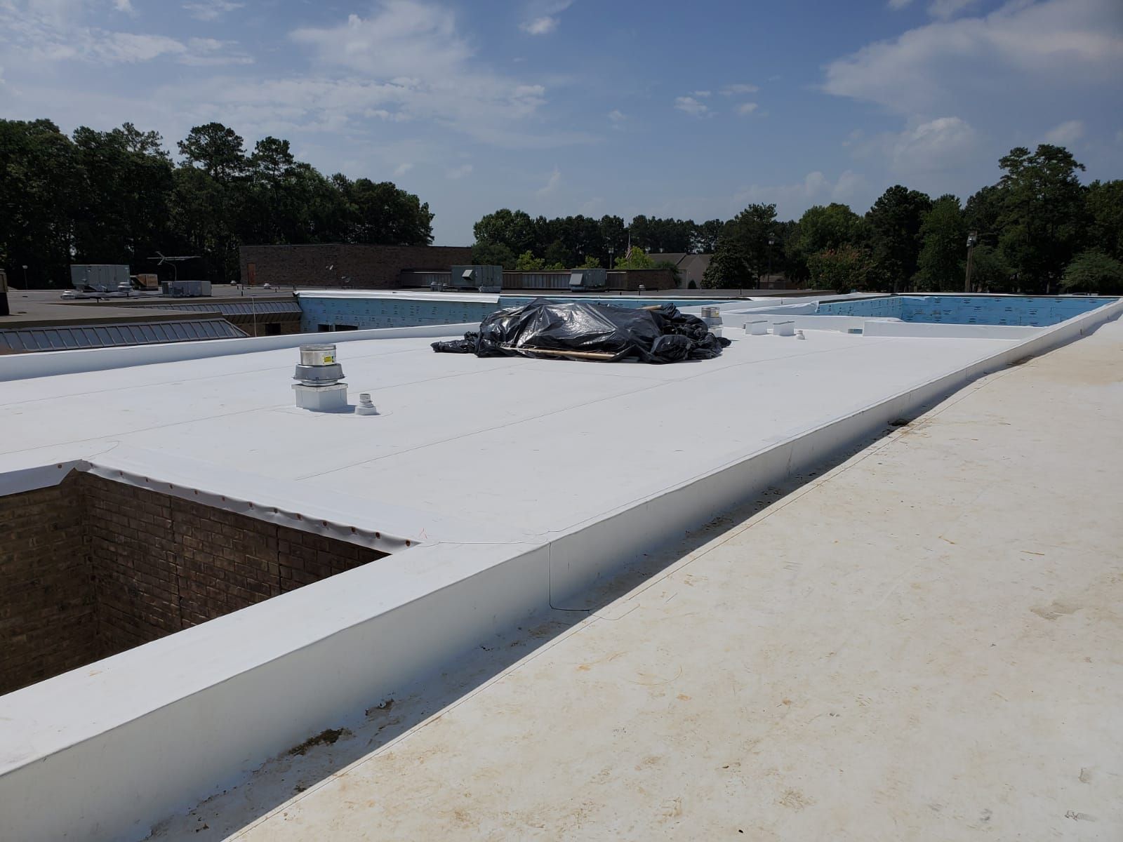 The roof of a building with a white roof and trees in the background.