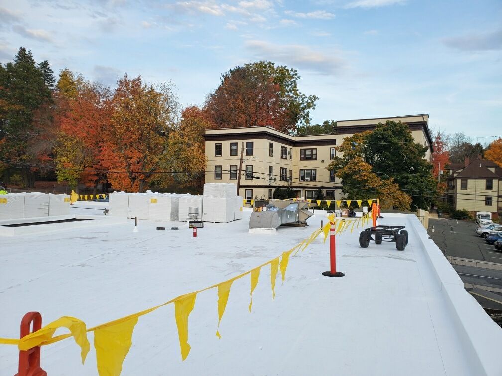 A white roof with yellow flags on it and a building in the background.
