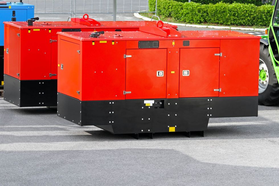 Two red industrial generators on a grey asphalt surface outdoors.