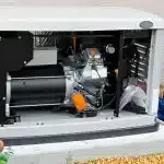An opened beige outdoor standby generator with an exposed internal engine and a bright orange oil filter.