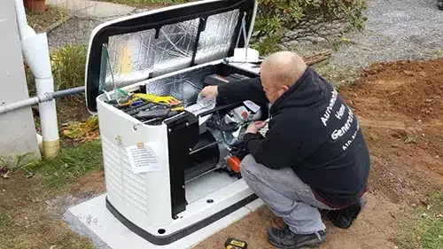 A service technician works on an open standby generator installed on a concrete pad outdoors.