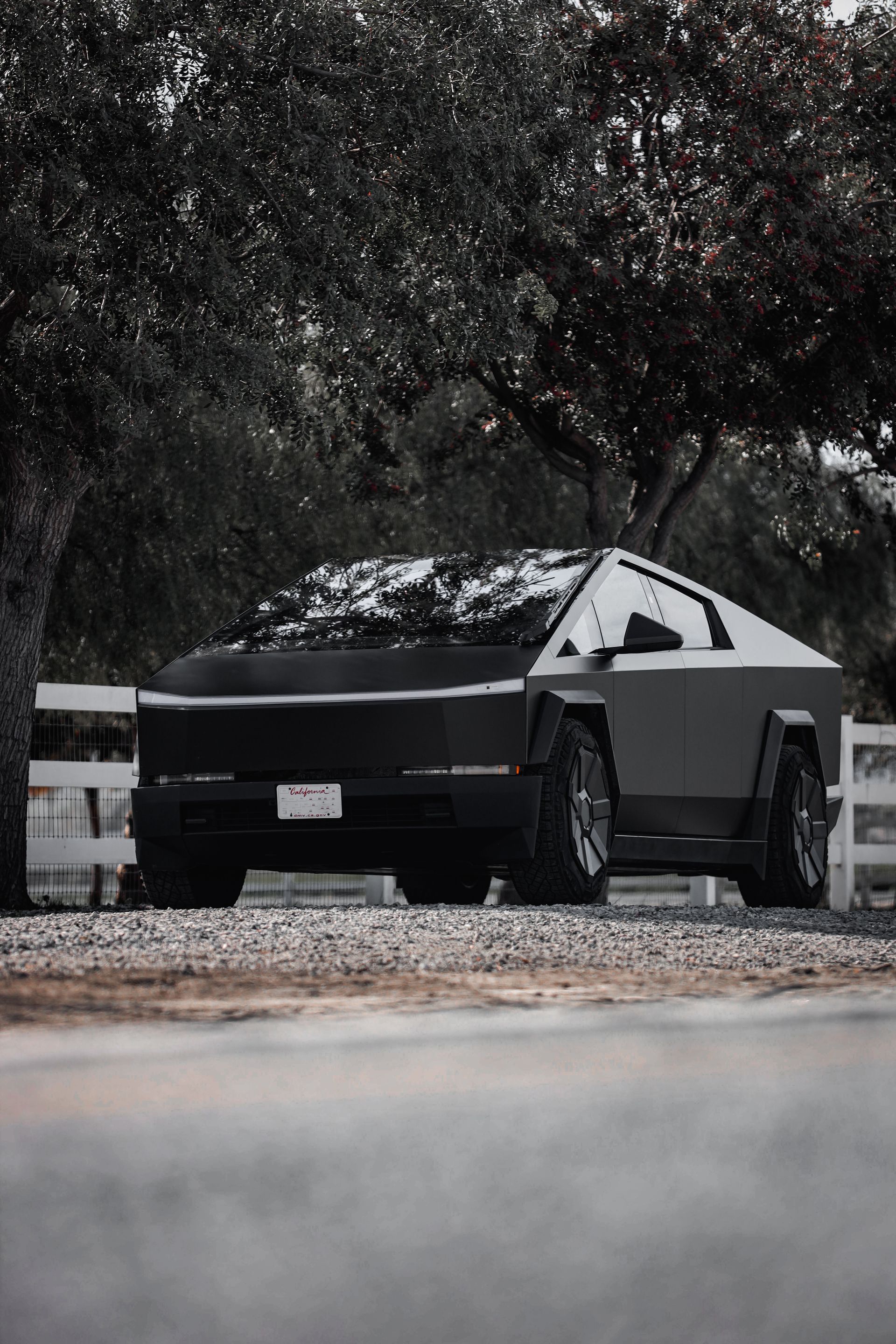 Tesla Cybertruck parked on a road. Dark, angular truck with a snowy windshield next to a white fence.