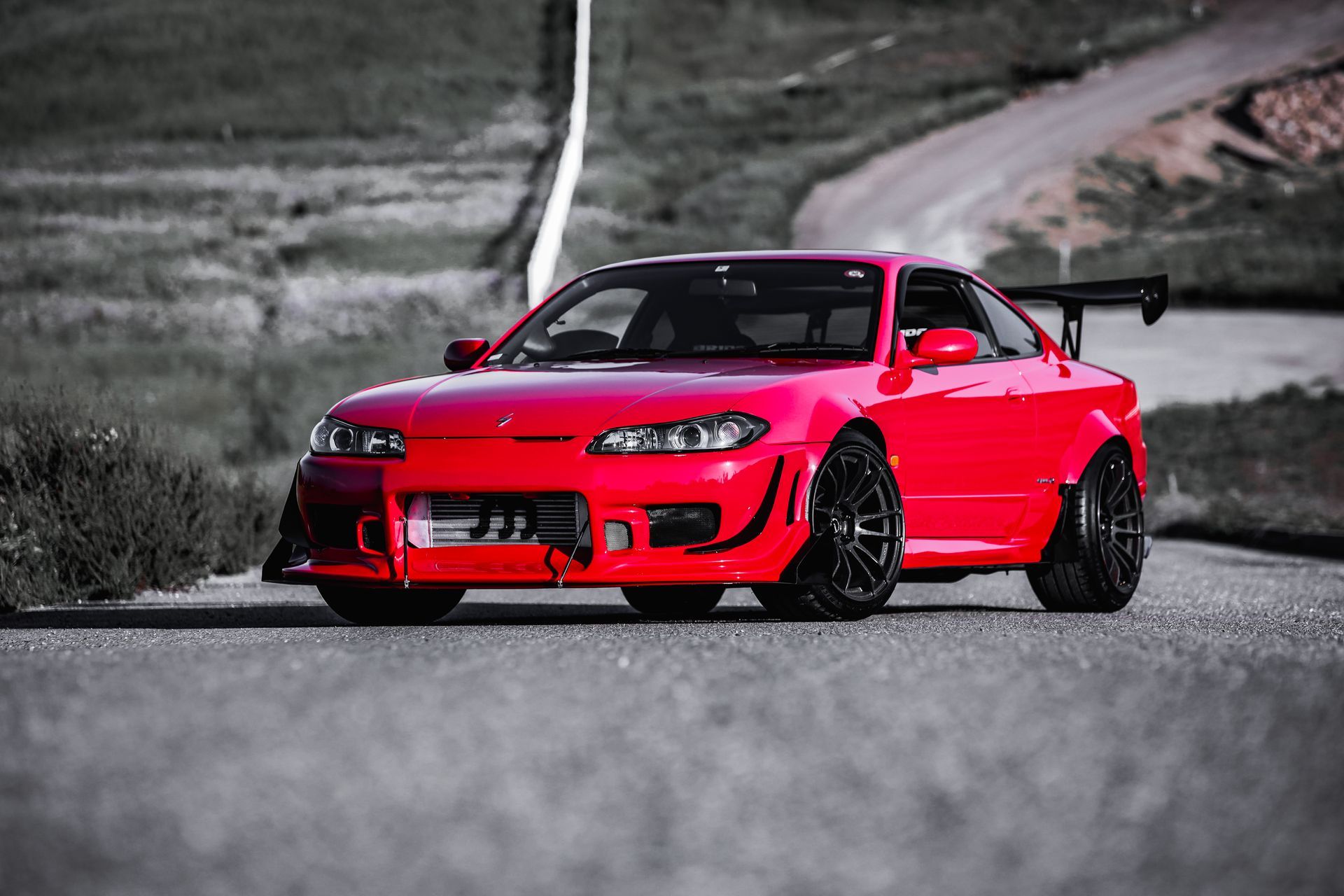 Red modified sports car on a winding road, with black wheels and a rear spoiler.