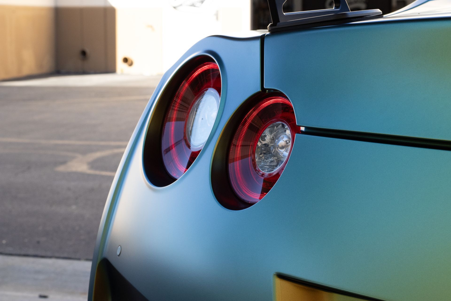 Close-up of a teal car's rear, showcasing its circular taillights with red outlines and a black spoiler.