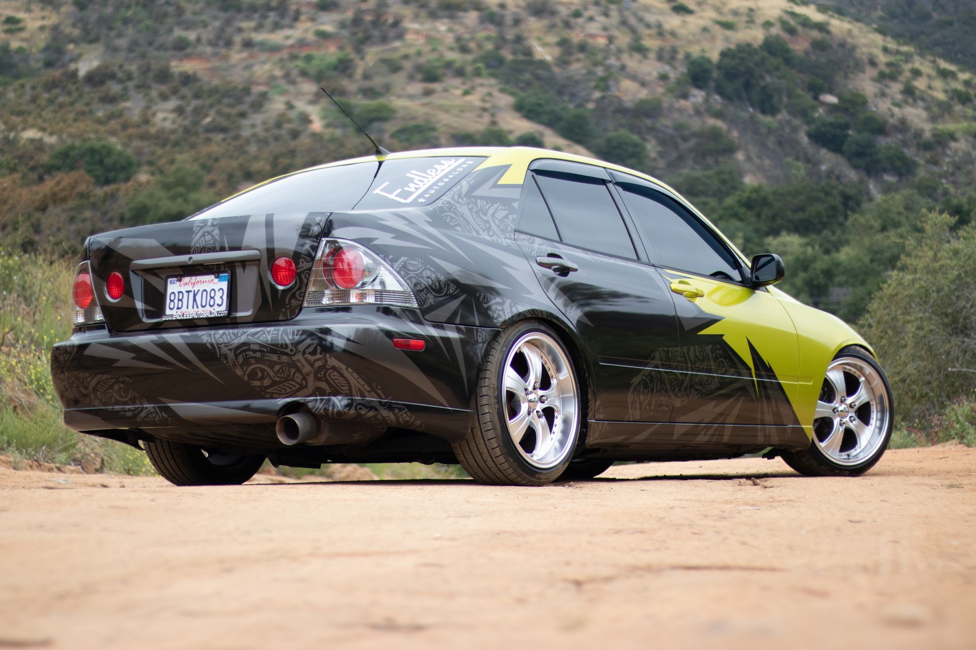 Modified black and lime green Lexus sedan on a dirt road, customized with chrome wheels and tinted windows.