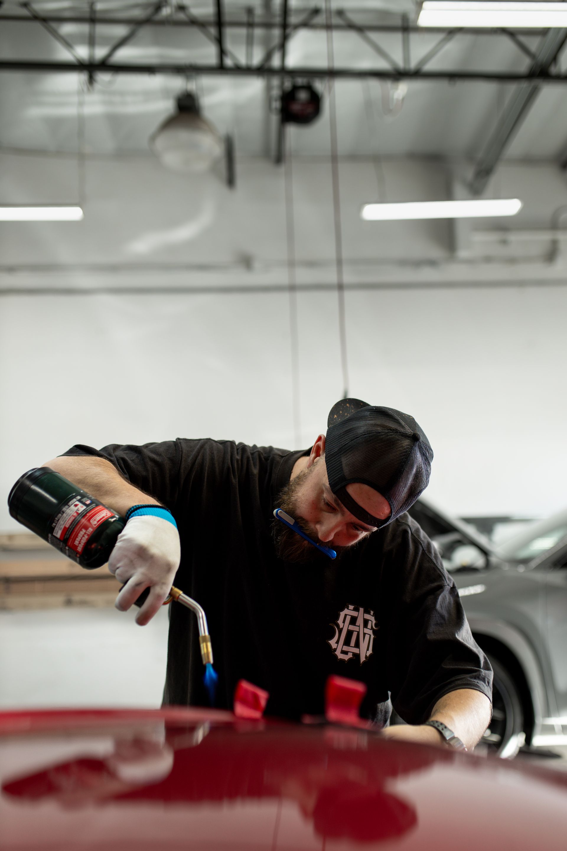 Man uses a torch on a red car in a shop.