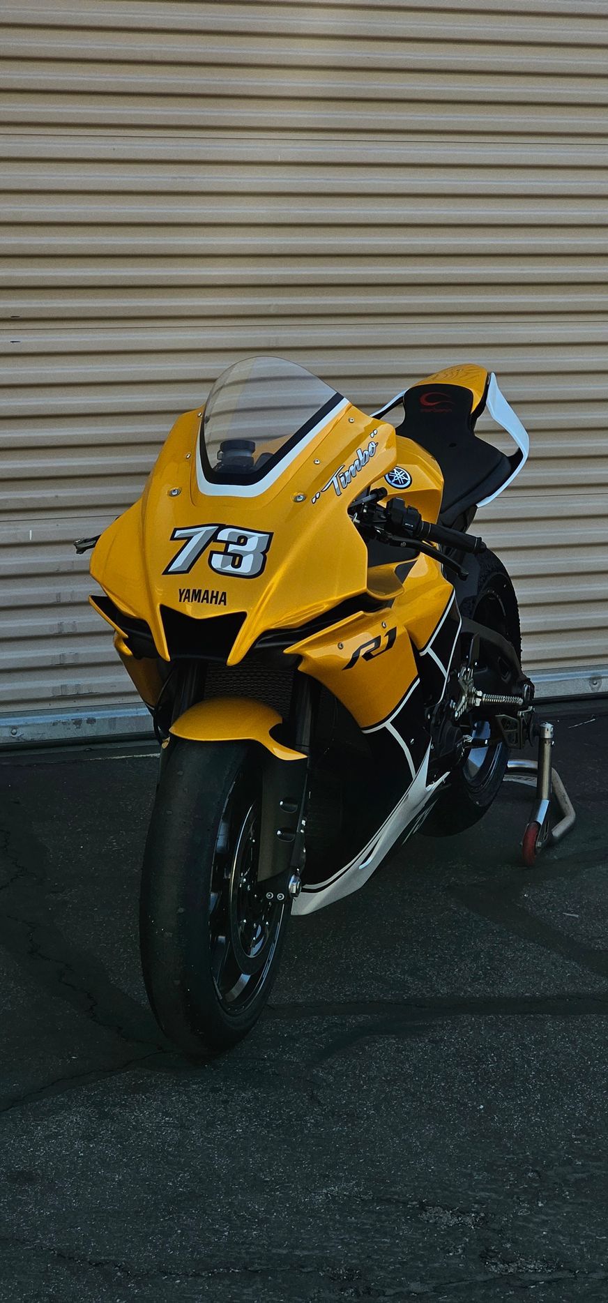 Yellow and black racing motorcycle parked in front of a closed garage door. Number 73 on the fairing.