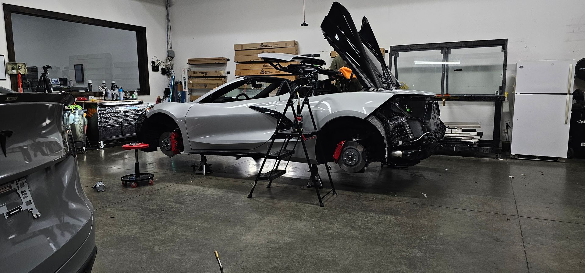 Silver convertible car in a garage, doors open, wheels off. Tripod in front of the car.