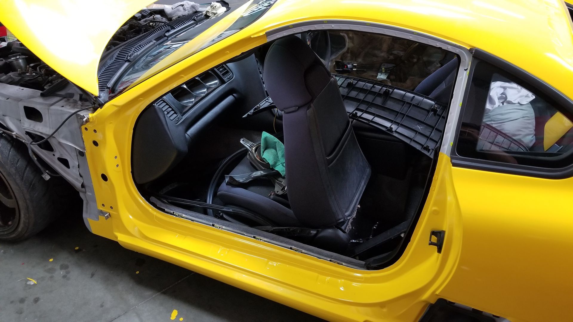 Yellow car's door open, exposing interior. The hood is up, revealing engine bay. Interior black seats.