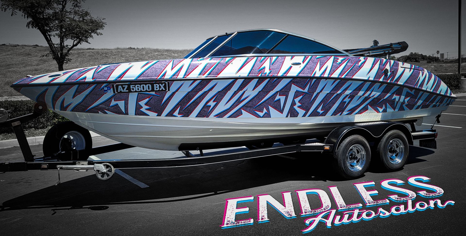 Boat with blue and white zebra print wrap on trailer in front of building; 