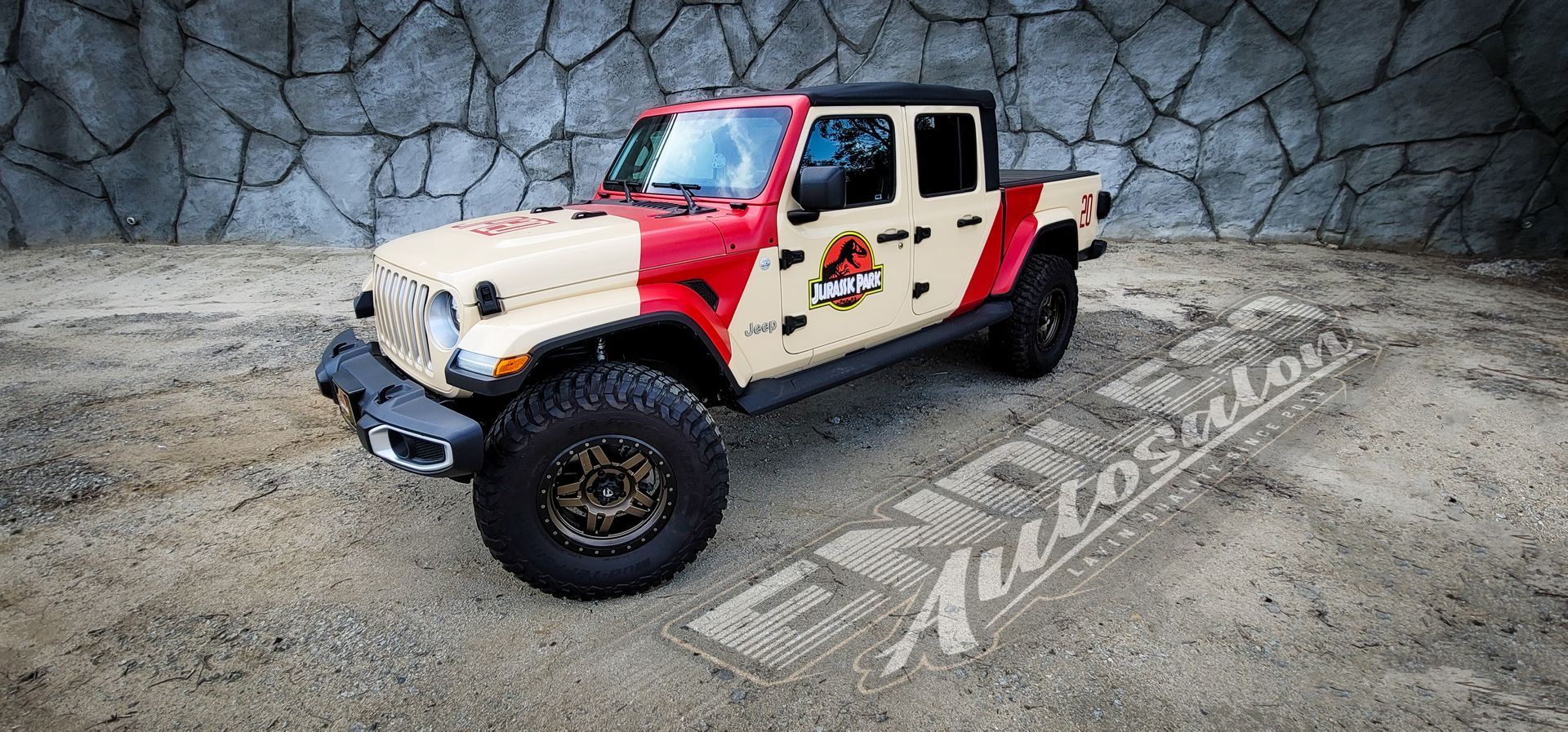Jurassic Park Jeep Gladiator truck on gravel with a stone wall backdrop.