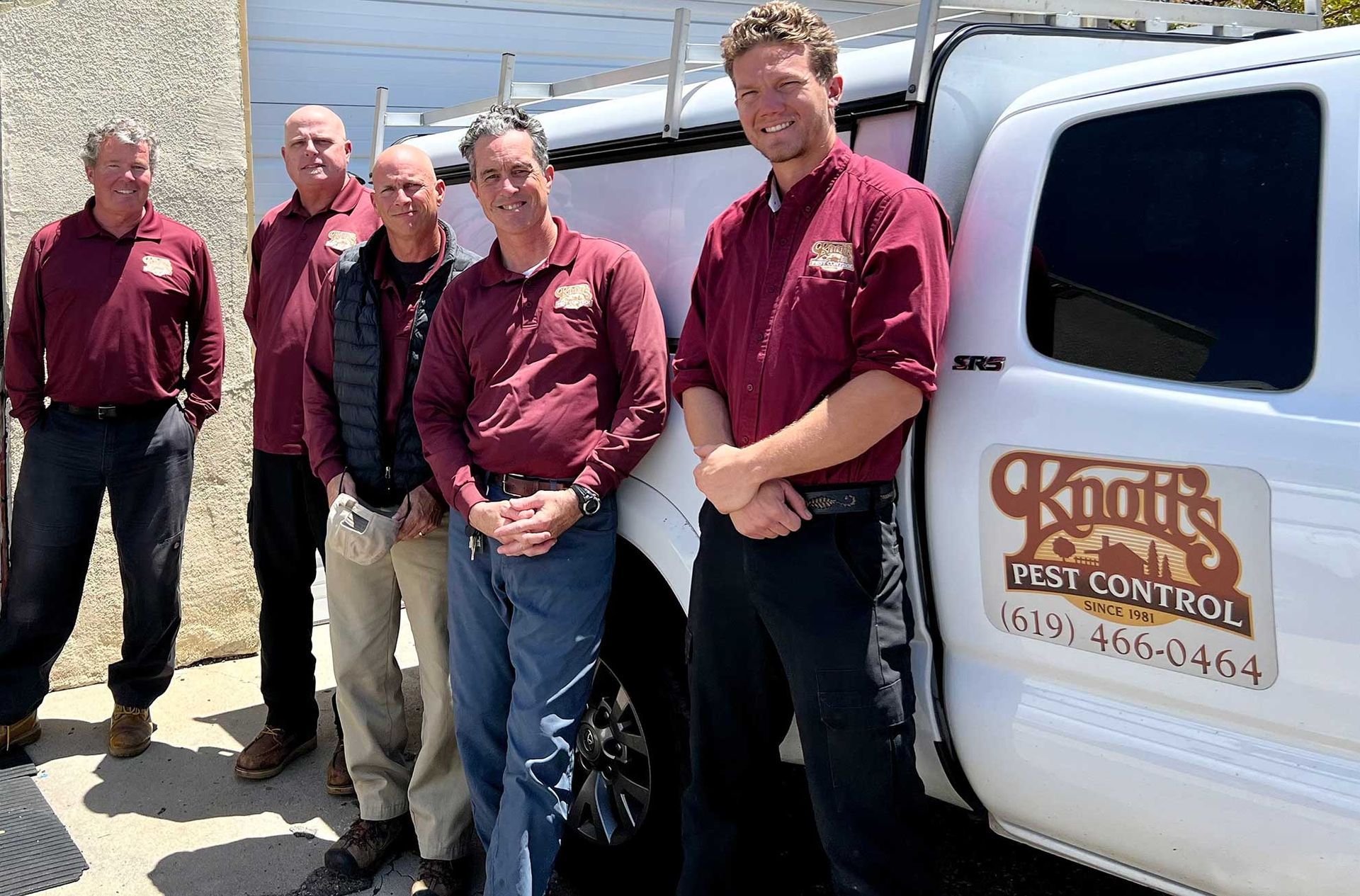 Six people wearing maroon shirts stand near a white truck with