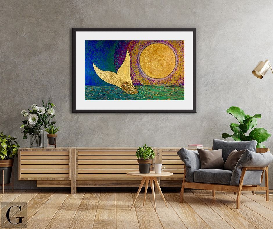 A framed art piece of a golden tail and sun over green water hangs on a grey wall.