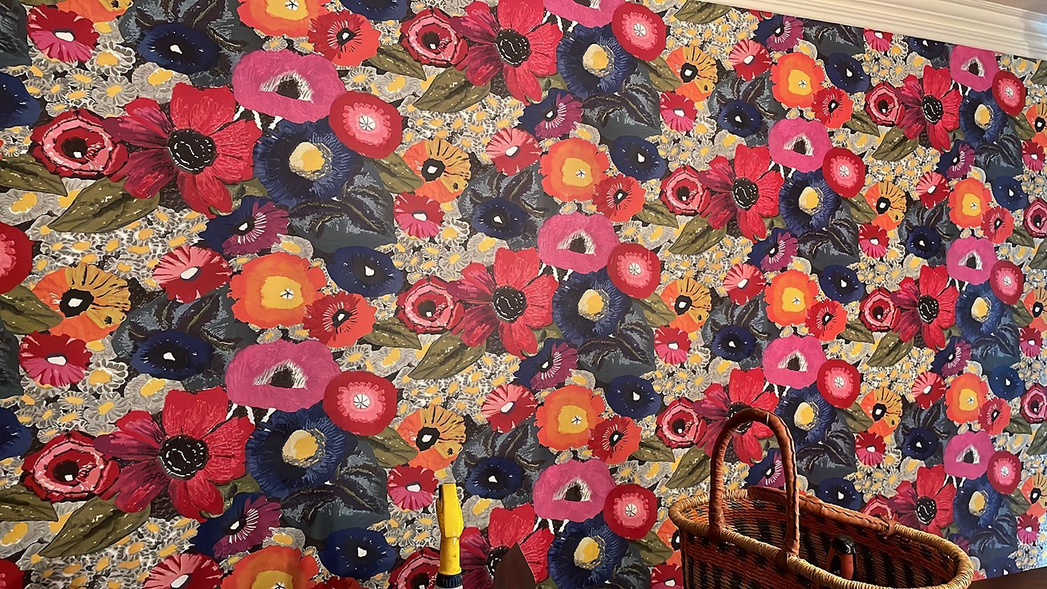 Wall covered in a vibrant floral wallpaper with red, pink, orange, and blue flowers. A wicker basket sits below.