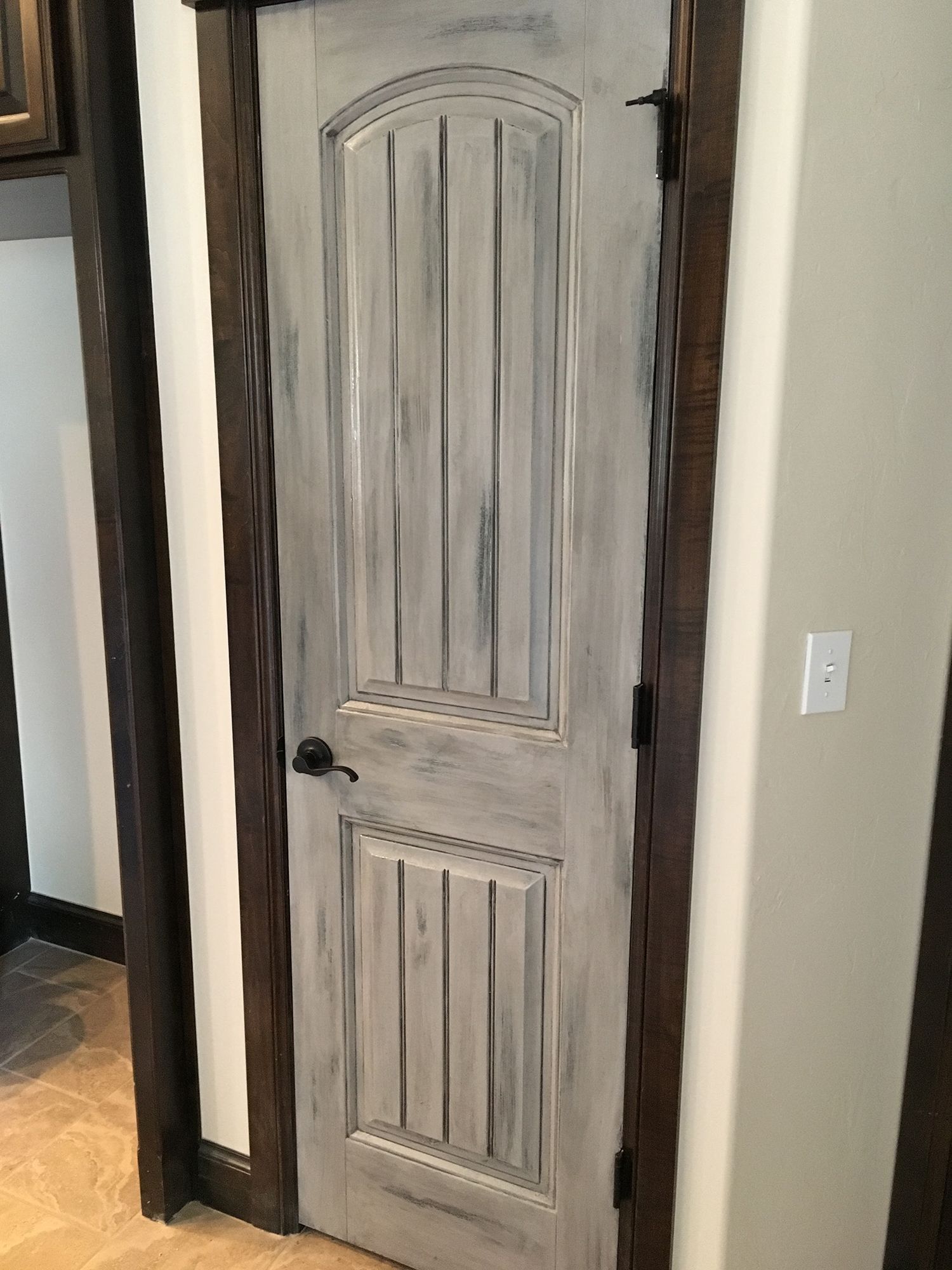 Gray-washed wooden door with vertical paneling, black hardware, framed by dark wood trim.