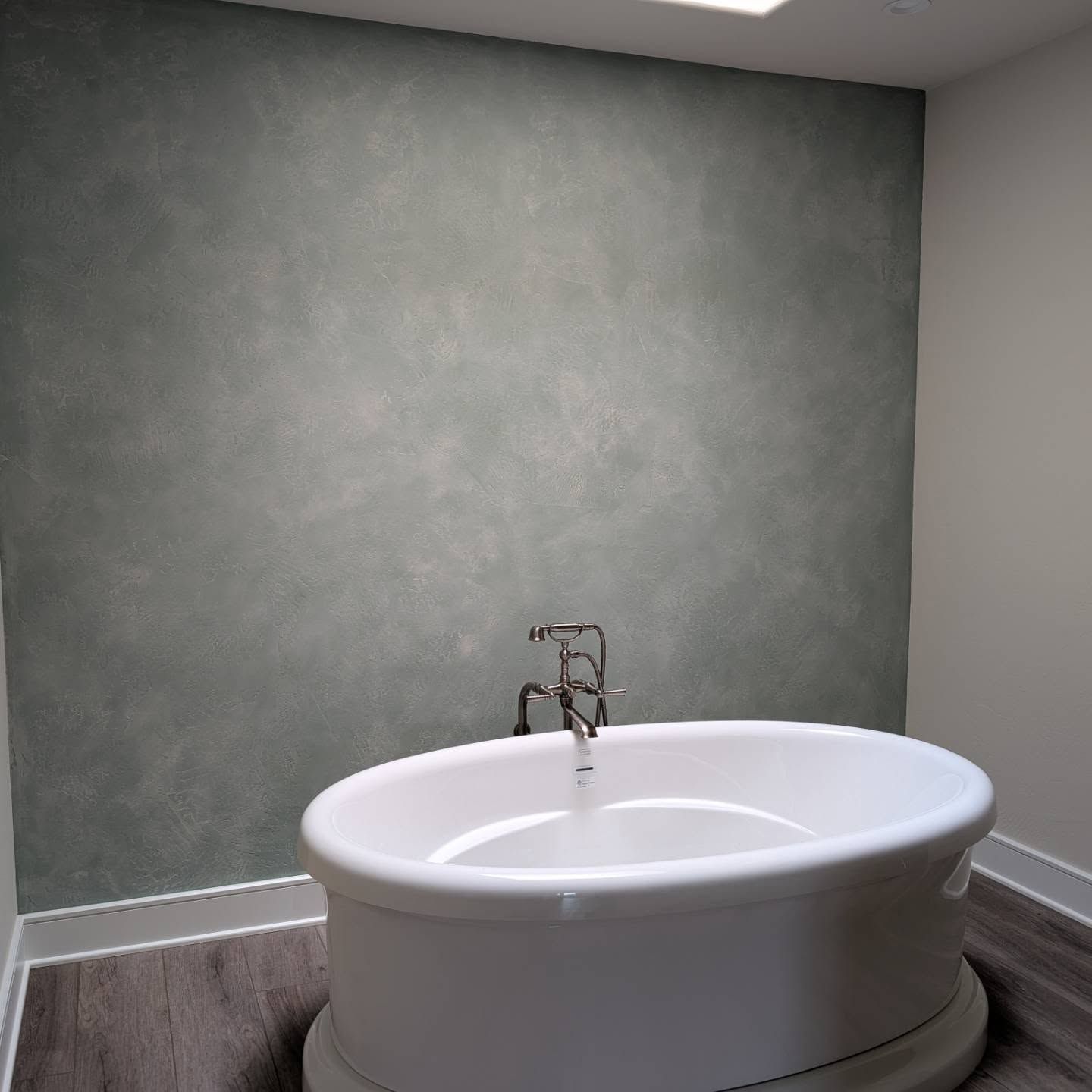 Oval bathtub in a bathroom with a mottled green wall and silver faucet.