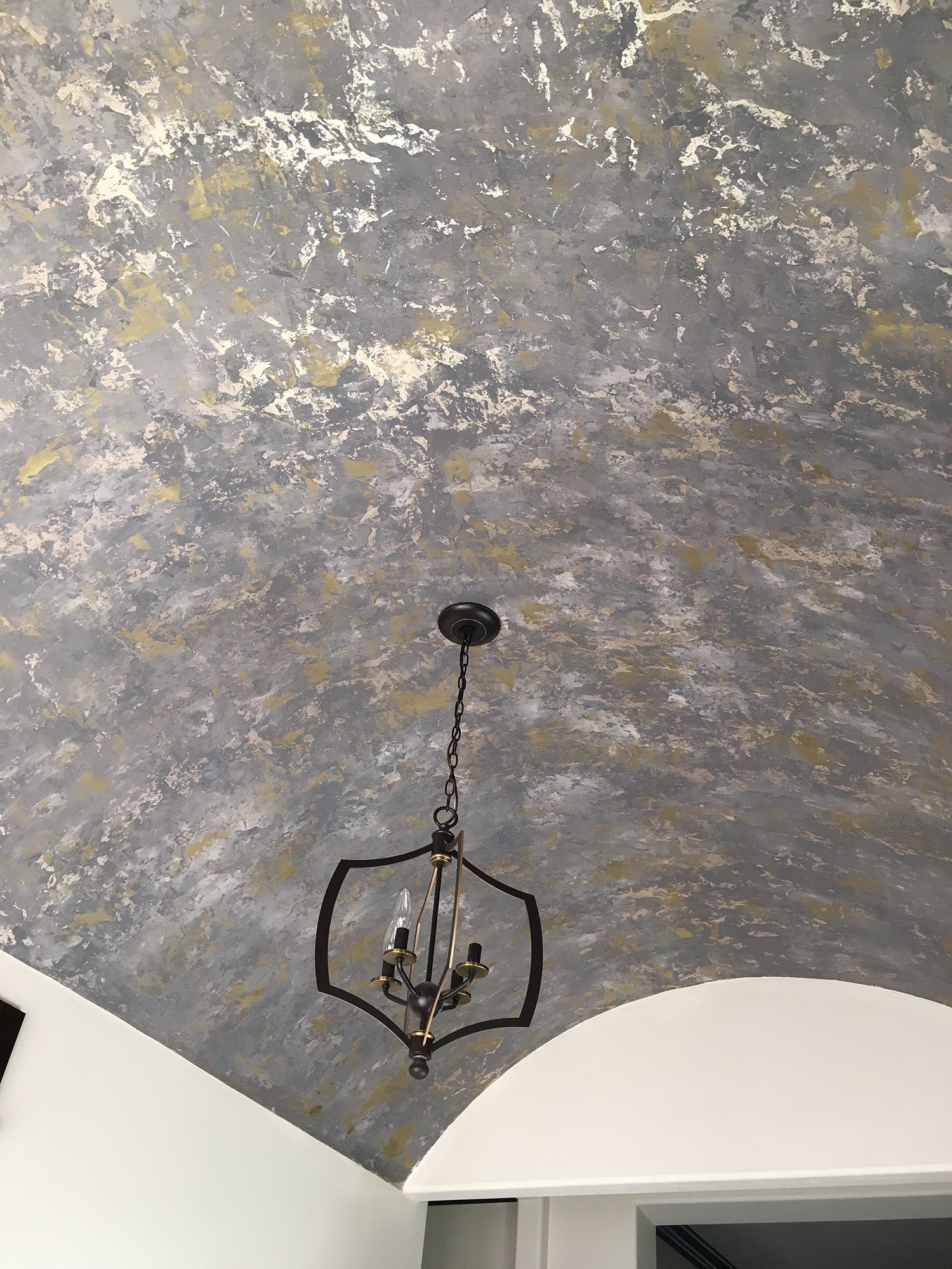 Textured gray and gold ceiling with chandelier. White arched doorway in foreground.