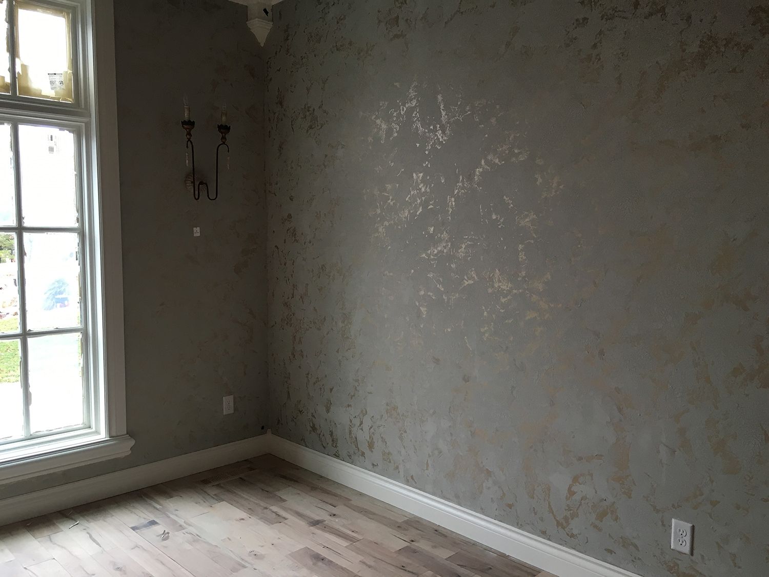Empty room with gray textured walls and gold accents, wooden floors, and a window.