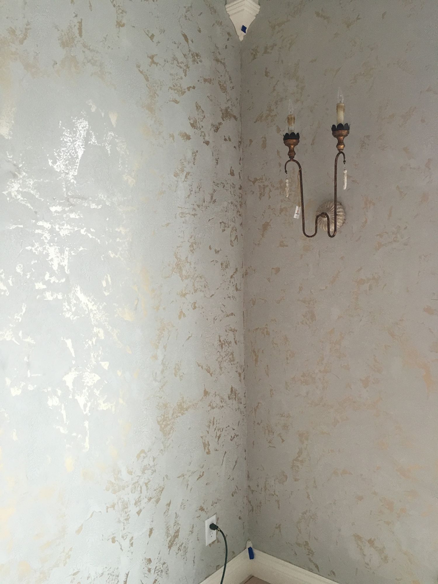 Light blue and gold textured walls with sconce and electrical outlet.