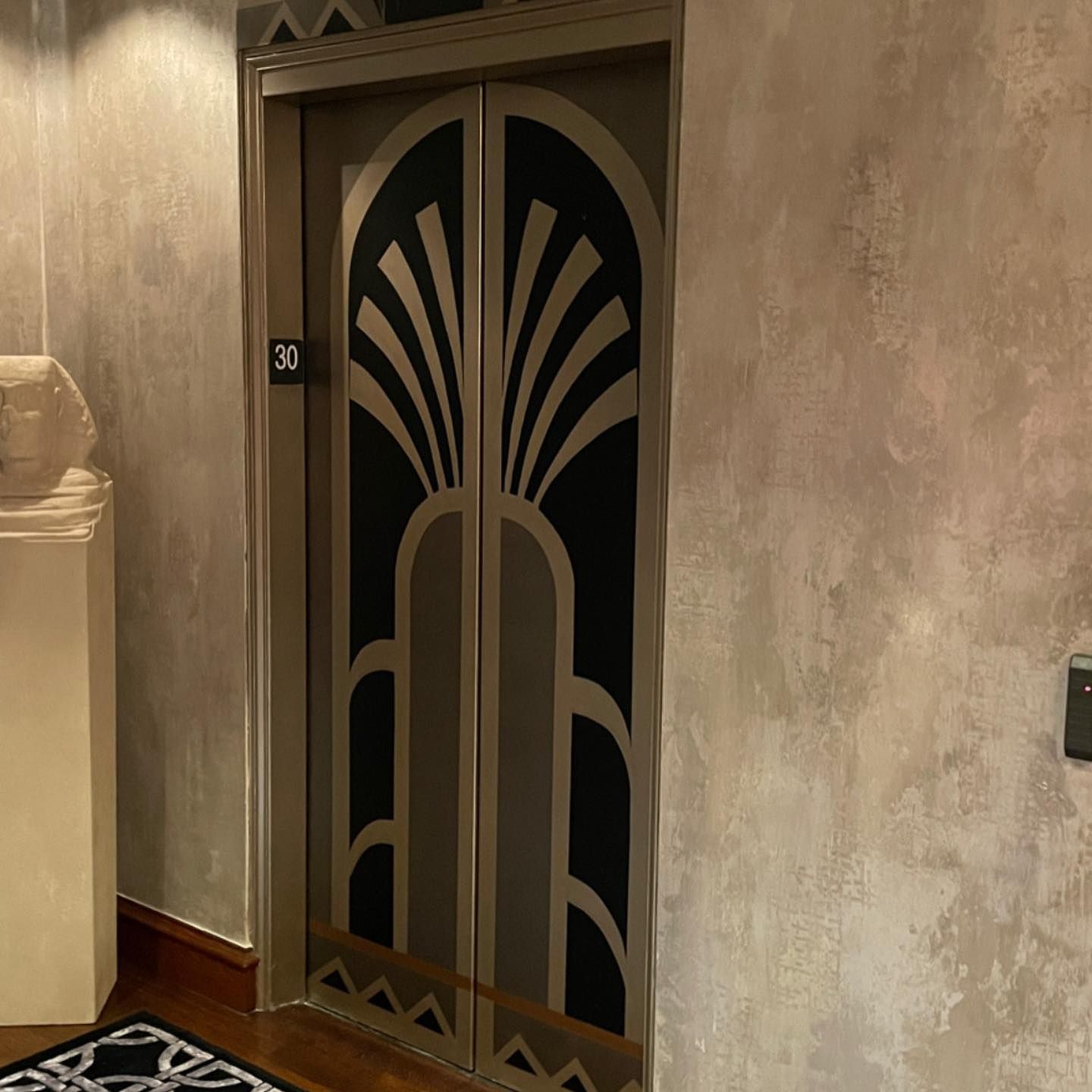 Art Deco elevator doors with black and gold details, set in a textured wall.