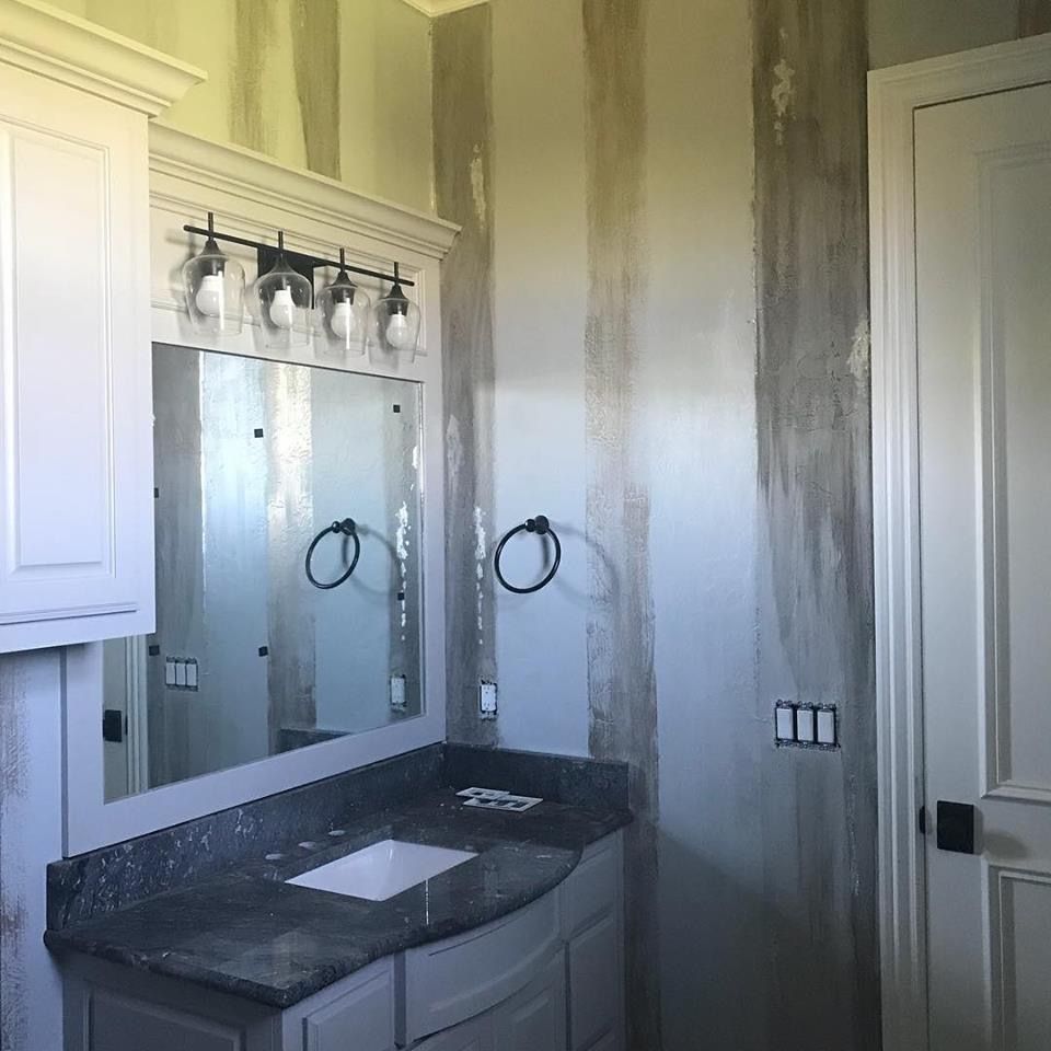 Bathroom with gray and white striped walls, vanity with gray countertop, and white cabinets.