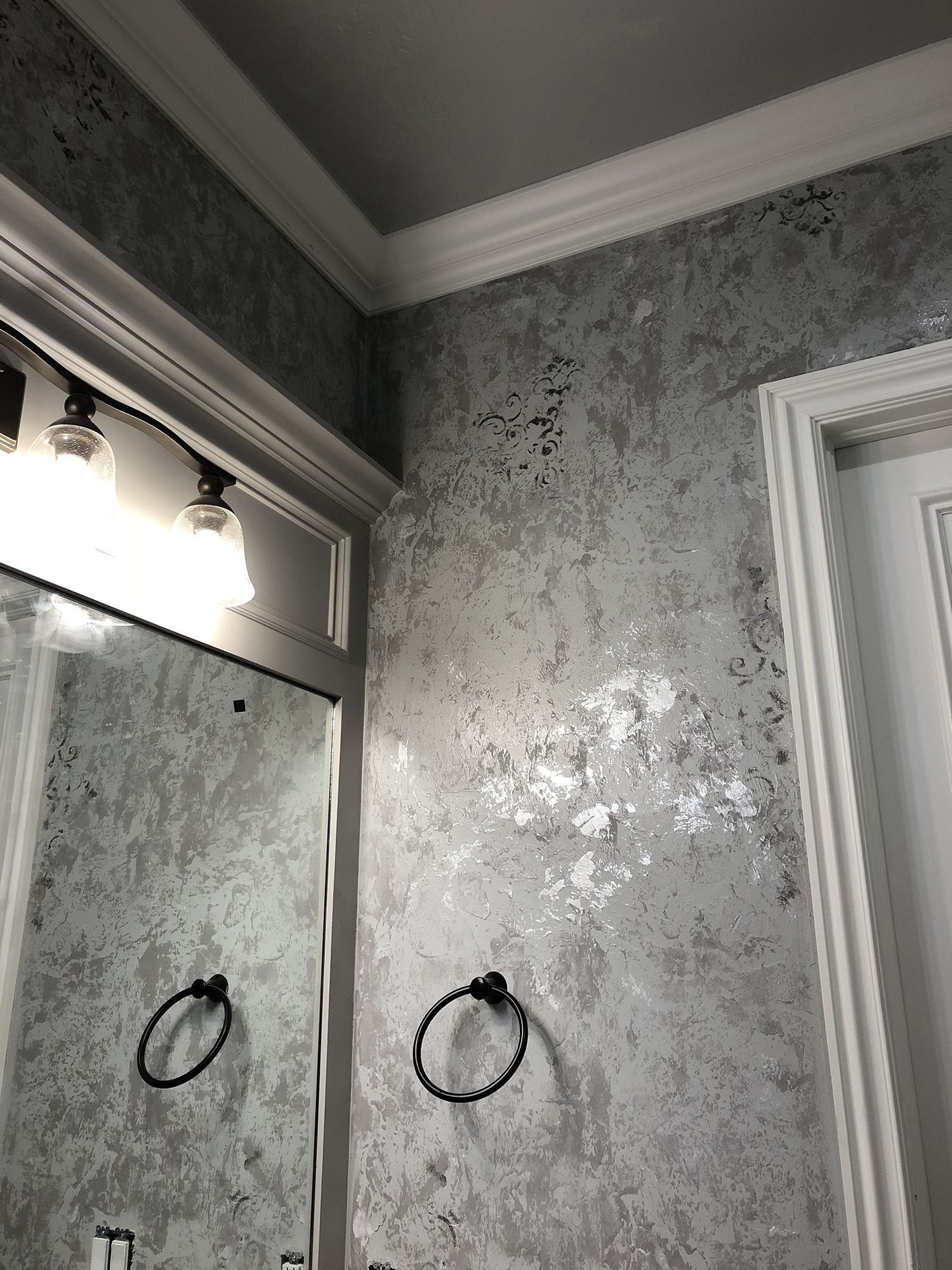 Bathroom with silver textured wallpaper, white trim, and a mirror.