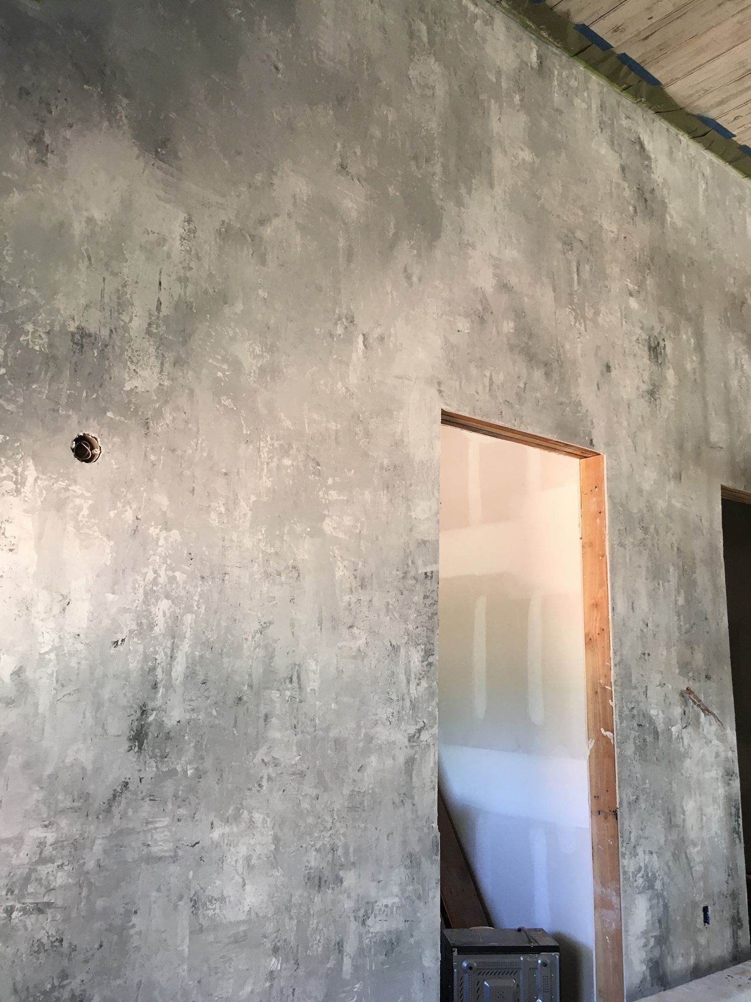 Textured gray interior wall with doorway and wood trim in a room under construction.