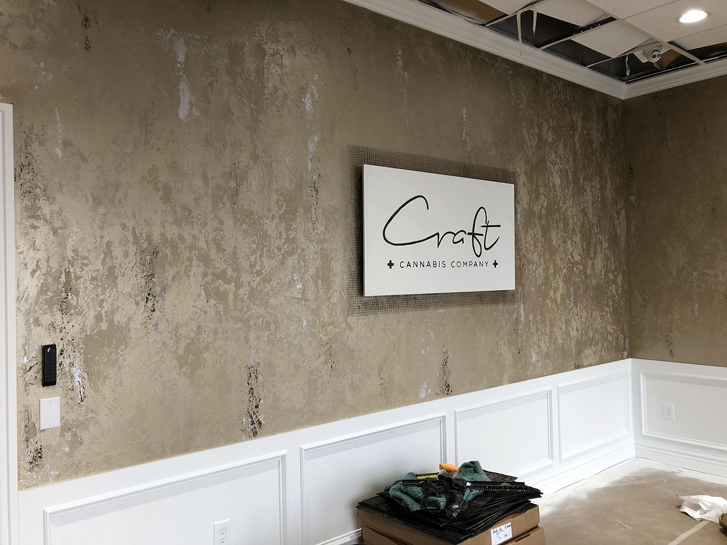 Wall with textured brown and silver finish, white wainscoting, and a sign.